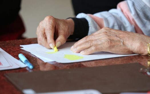mani di una signora anziana che sta colorando con dei pastelli in una casa di risposo